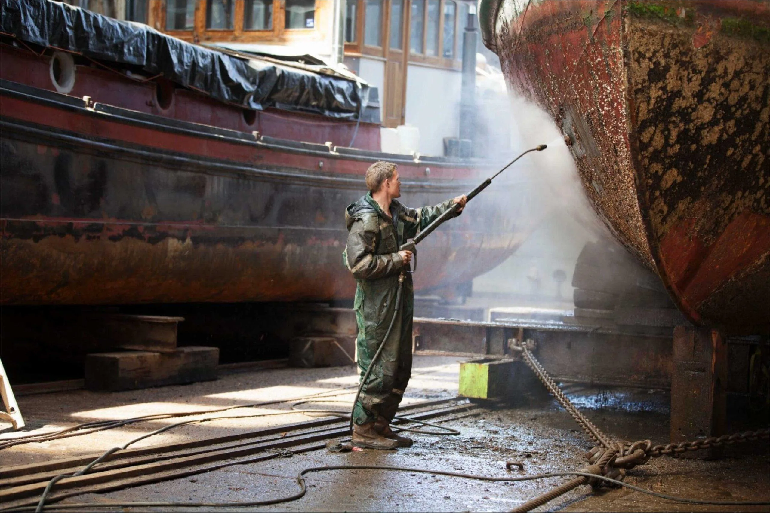 A dockworker sprays a boat with high pressure water to clean its underside.