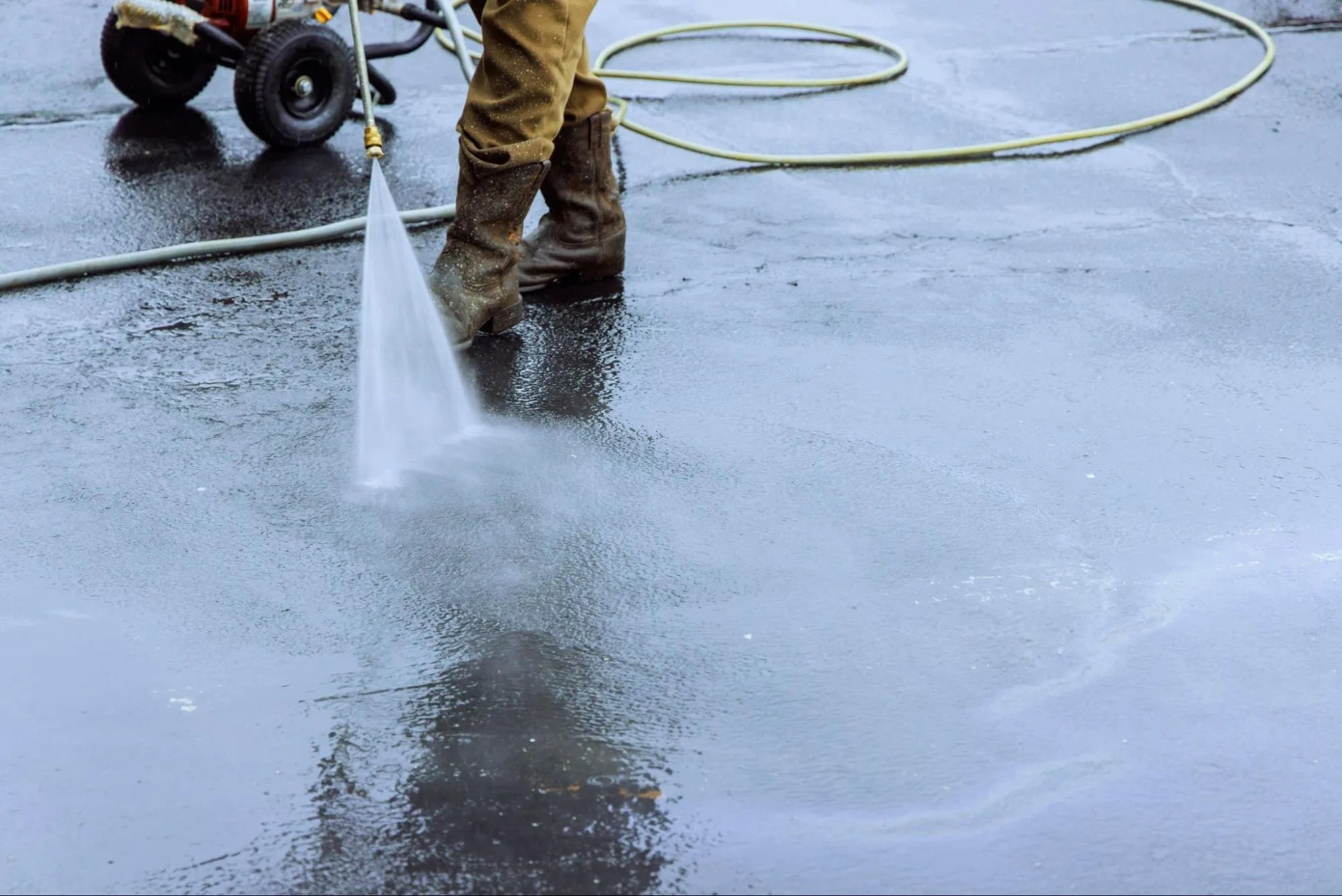 A close-up of a worker power washing a parking lot.