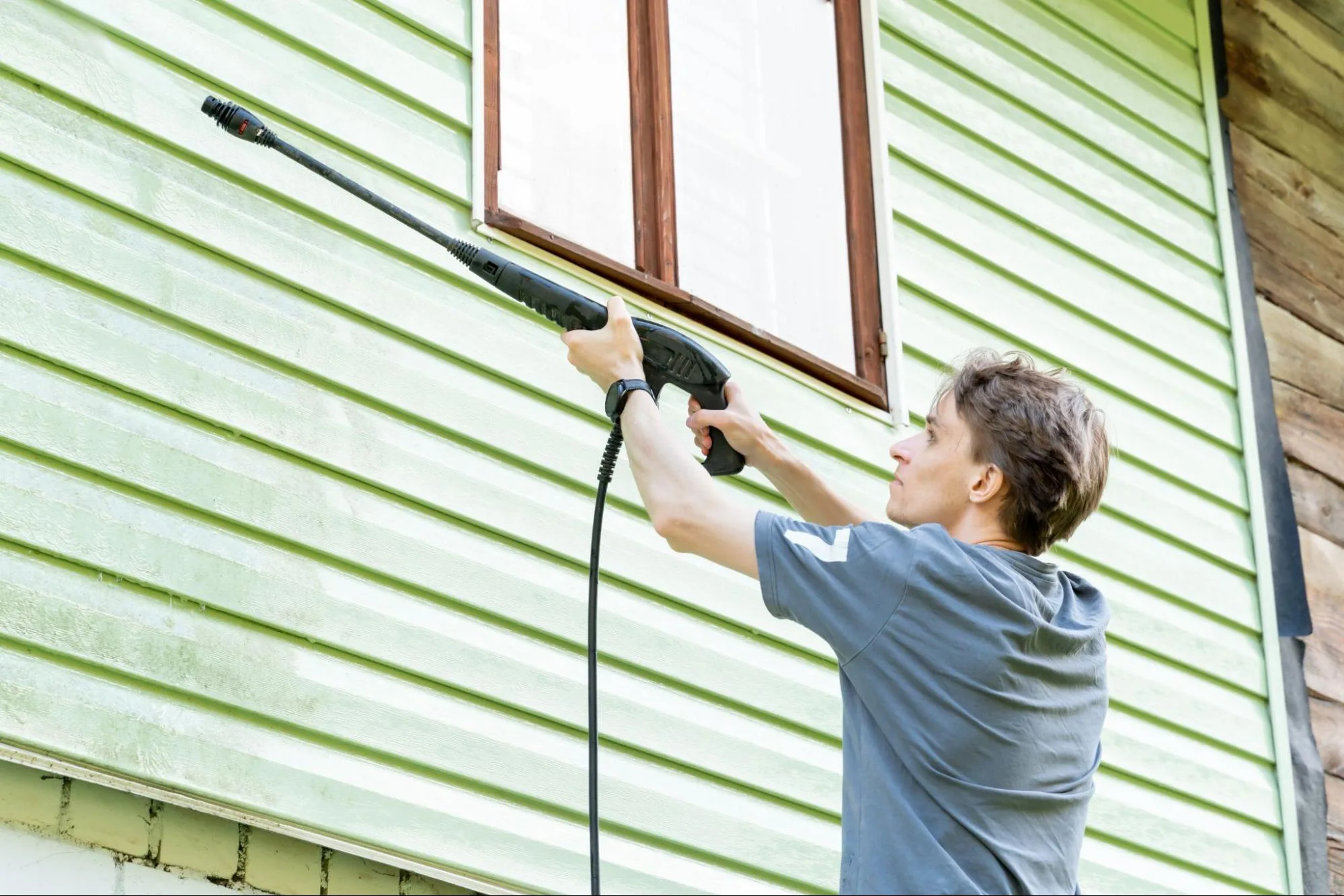 A homeowner uses gloved hands to remove leaves from their gutters.